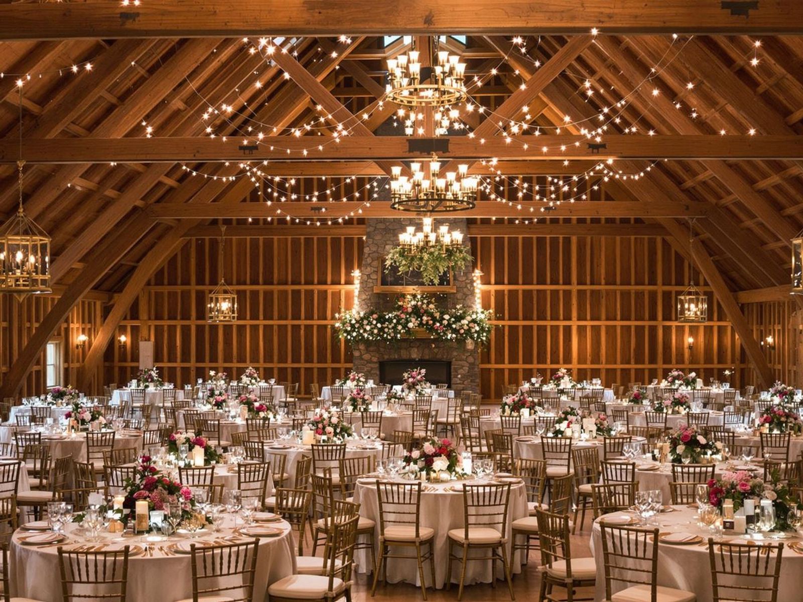 Large timber hall arranged with round dining tables, flowers, and chandeliers.