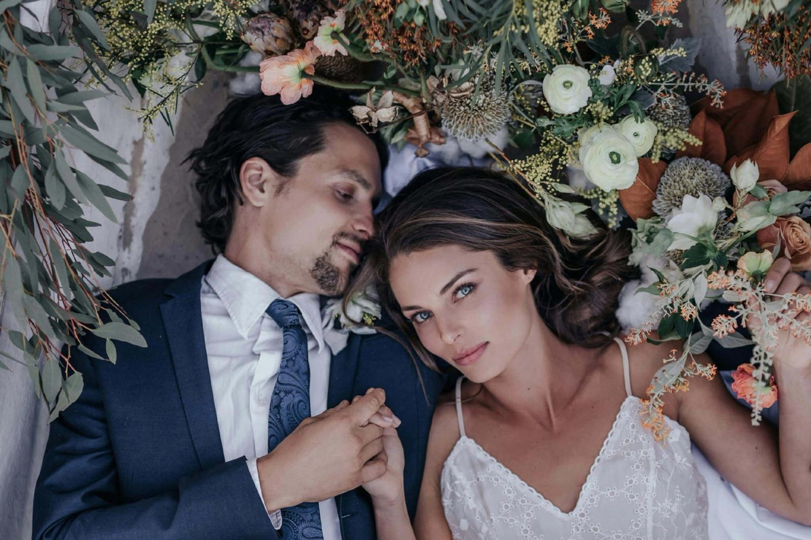 Overhead portrait of a couple lying beside flowers and greenery.