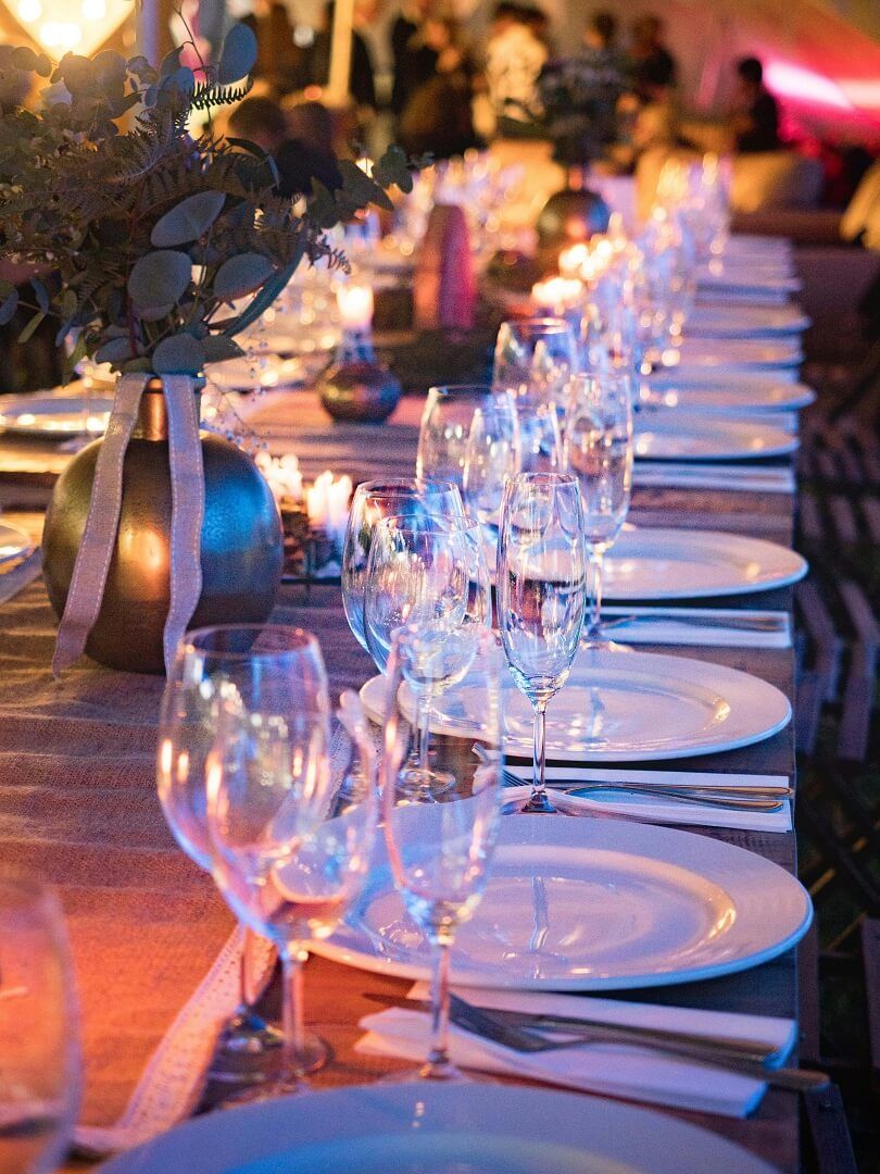 Long Table Setting Long dining table set with white plates, glassware, candles, and greenery.