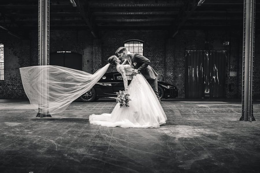 Industrial Hall Portrait Black-and-white wide portrait of a couple embracing inside an industrial hall, with a long veil extended.