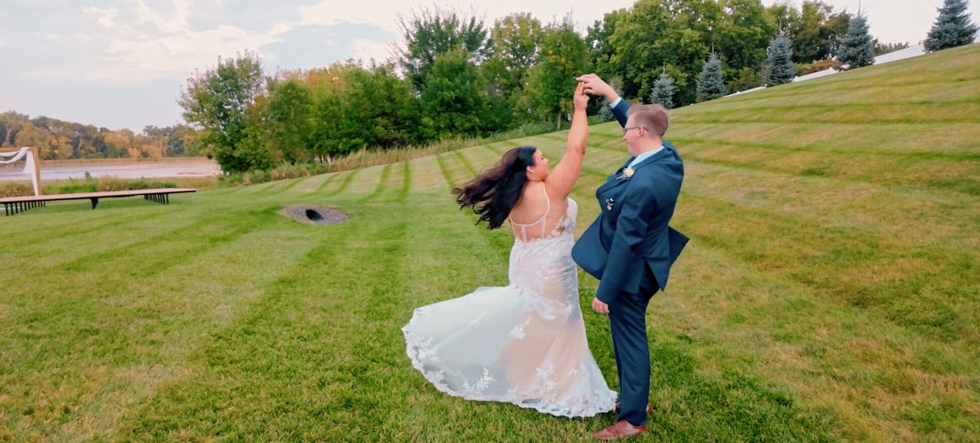 Two people in formal clothing holding hands on a grassy slope, one leaning backward.