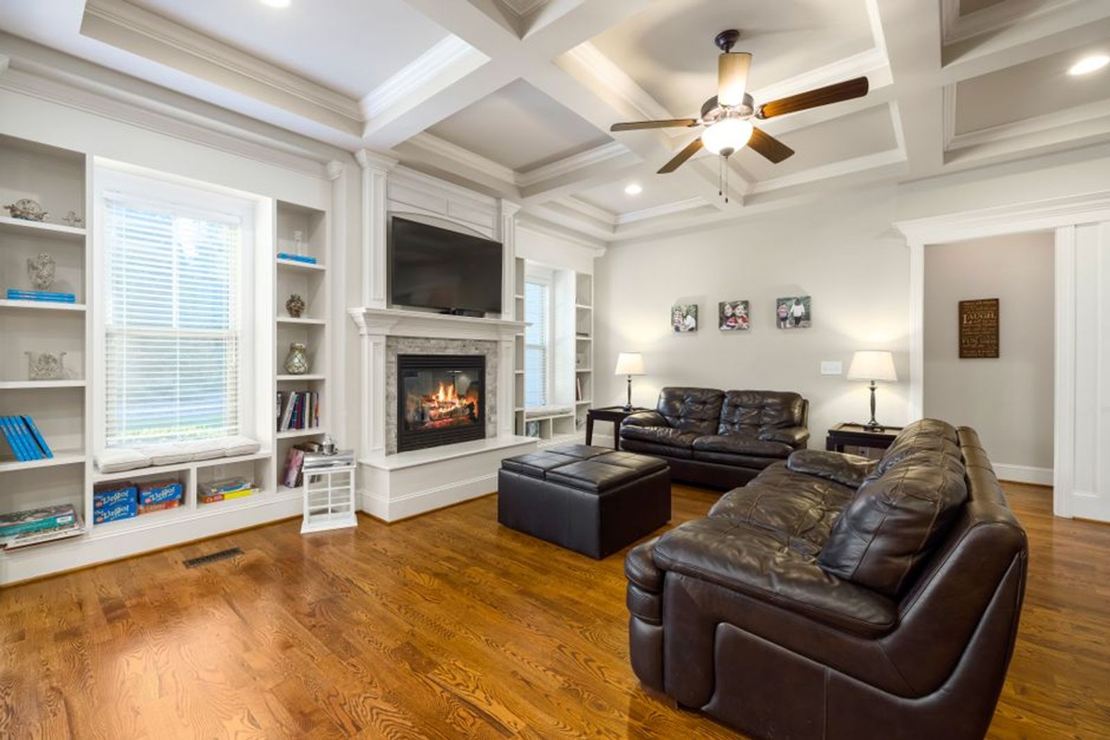 Bright living room with leather sectional seating, fireplace, windows, and wood floor.