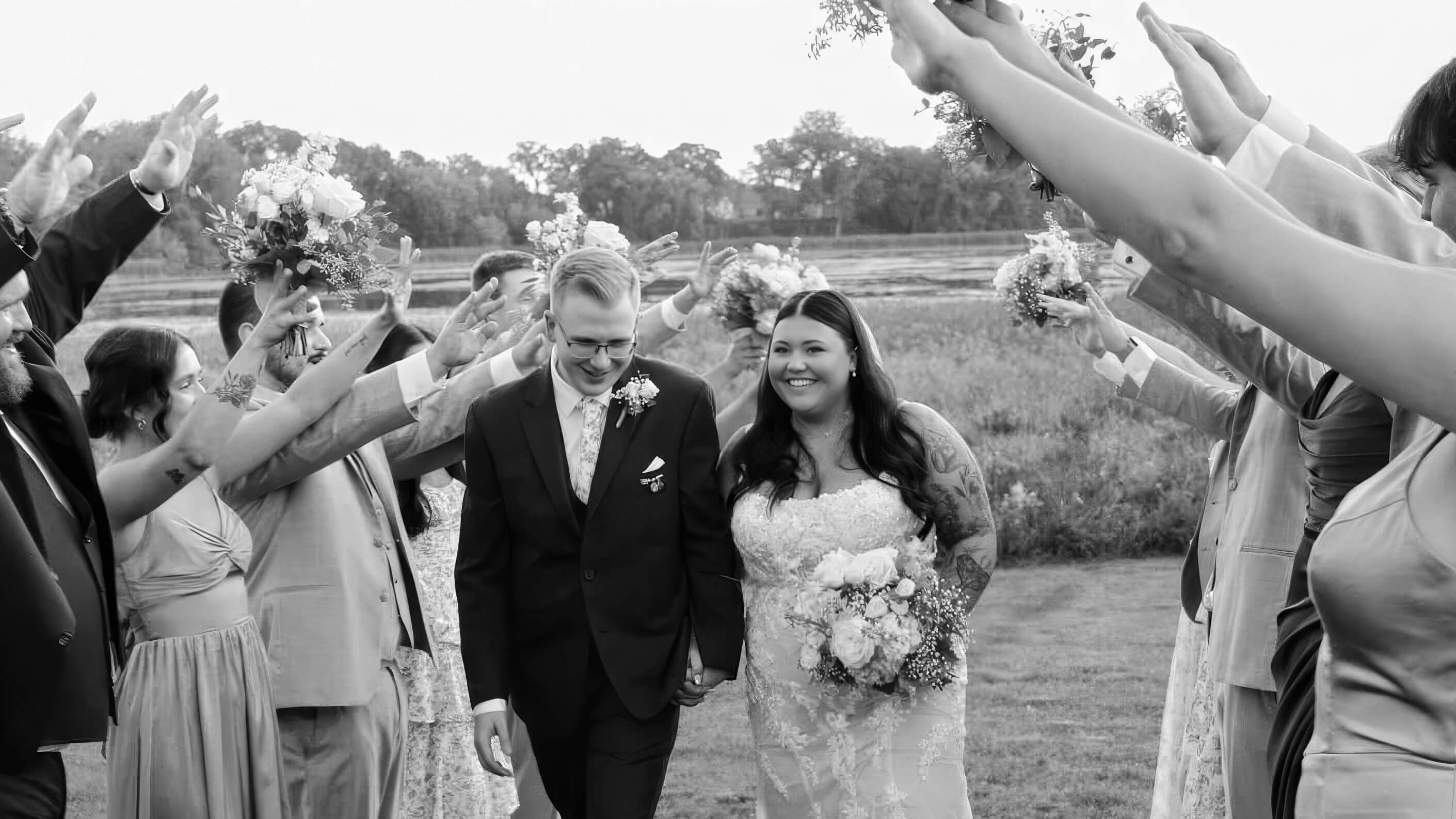 Black-and-white image of two formally dressed people walking between raised arms.