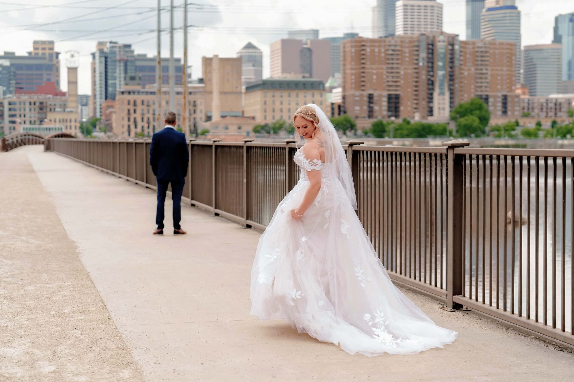 Skyline Bridge Person in a white dress and person in a dark suit standing apart on a bridge with a skyline behind.