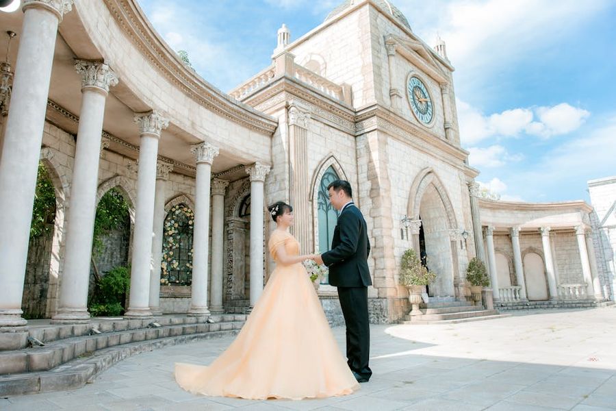 Columned Building Portrait Couple in formal clothing standing before a large white building with columns and a clock tower.