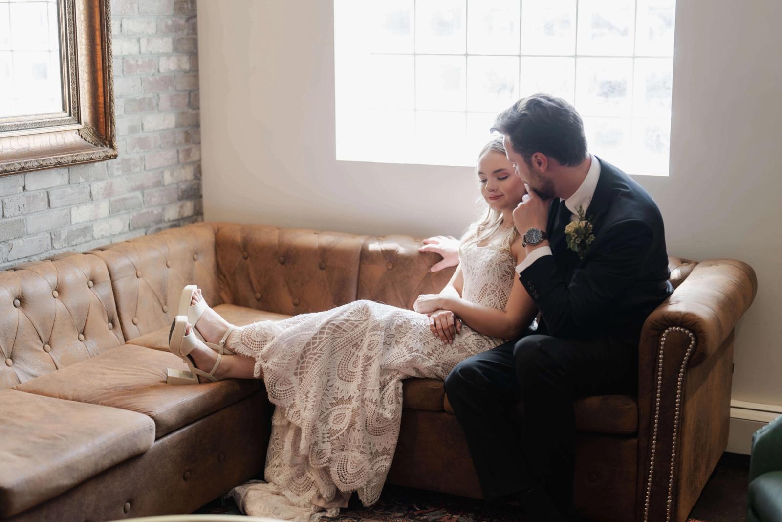 Couple in formal clothing seated closely on a brown leather sofa.