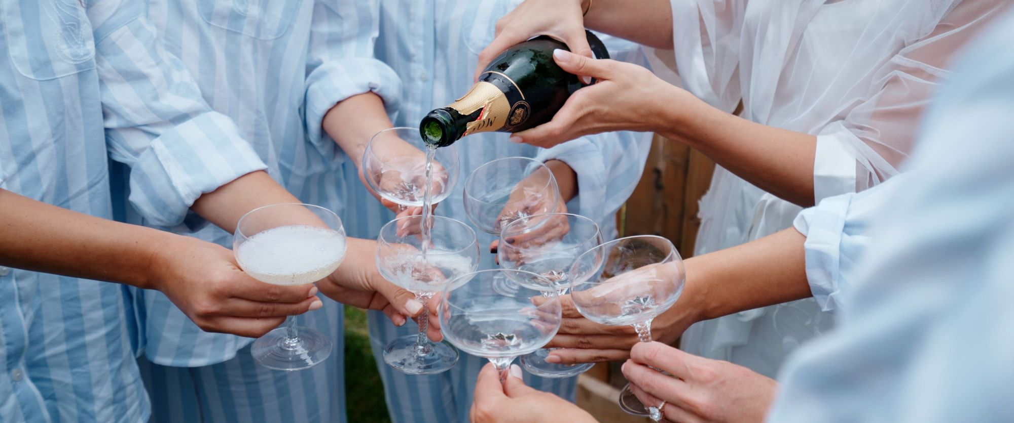 Sparkling Wine Pour Hands pour sparkling wine into clustered stemmed glasses held by several people.