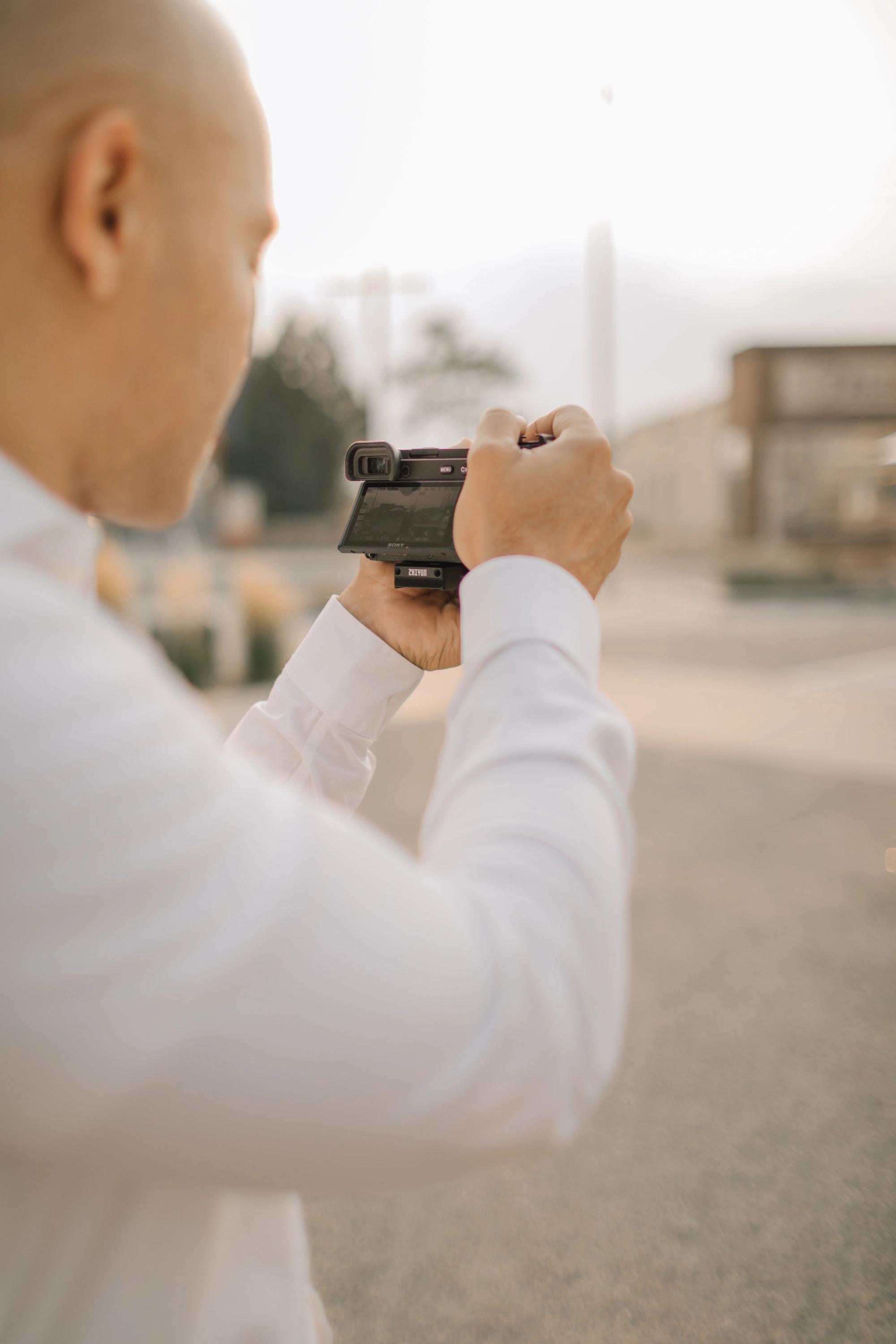 Small Camera Person in a white shirt holding a small camera outdoors.