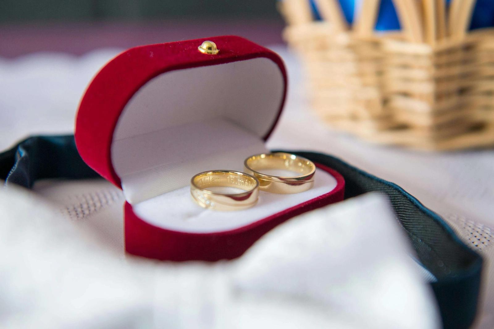 Two gold rings rest in an open red velvet ring box on white fabric.