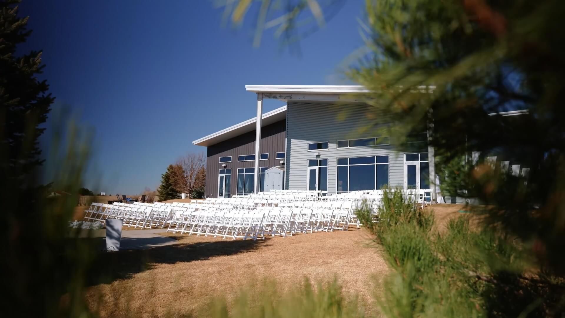 Lawn Chair Rows Rows of empty white chairs on a lawn facing a modern building beneath a dark blue sky.