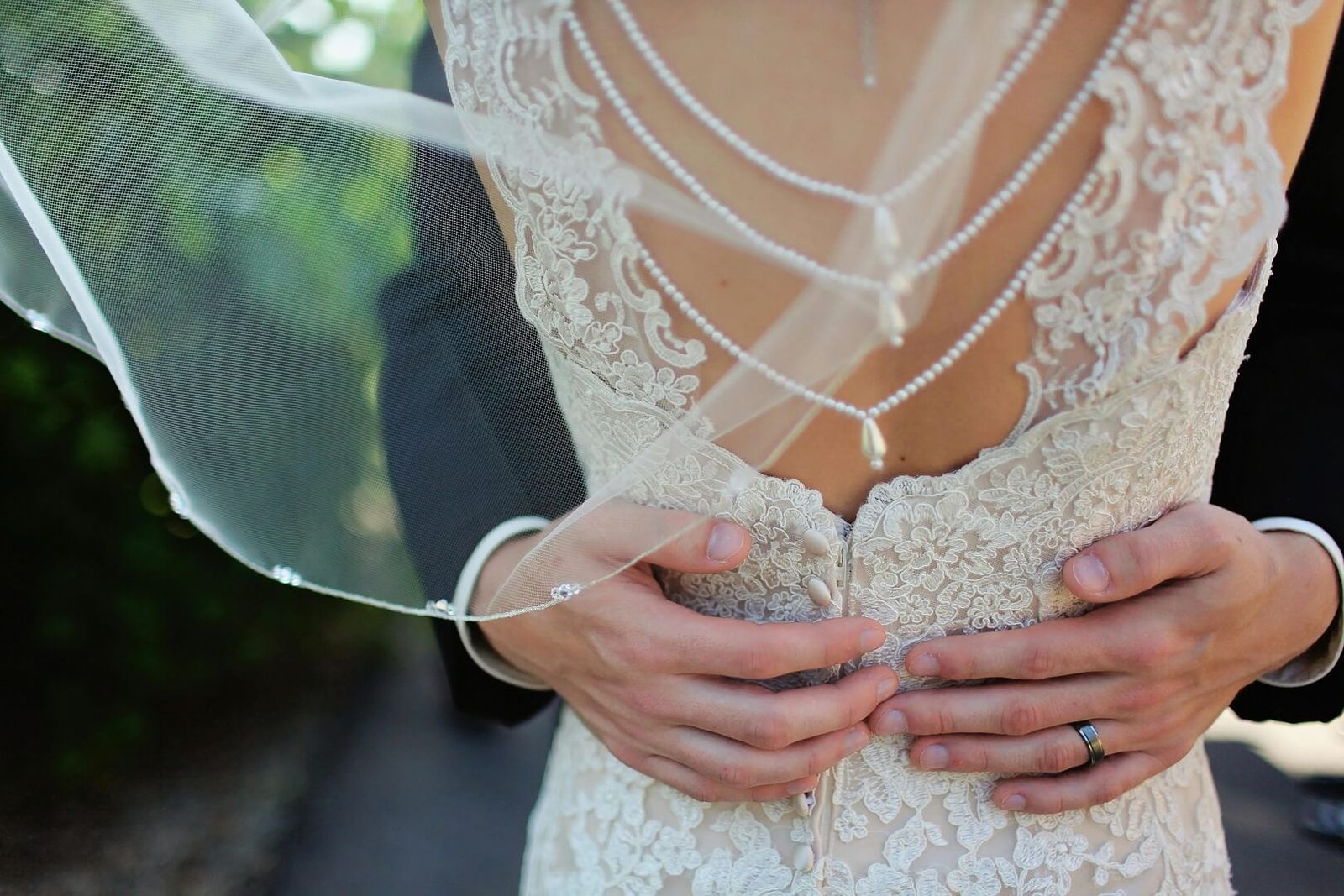 Pearl Back Detail Close crop of hands around the waist of a person wearing a lace dress and pearl back chains.