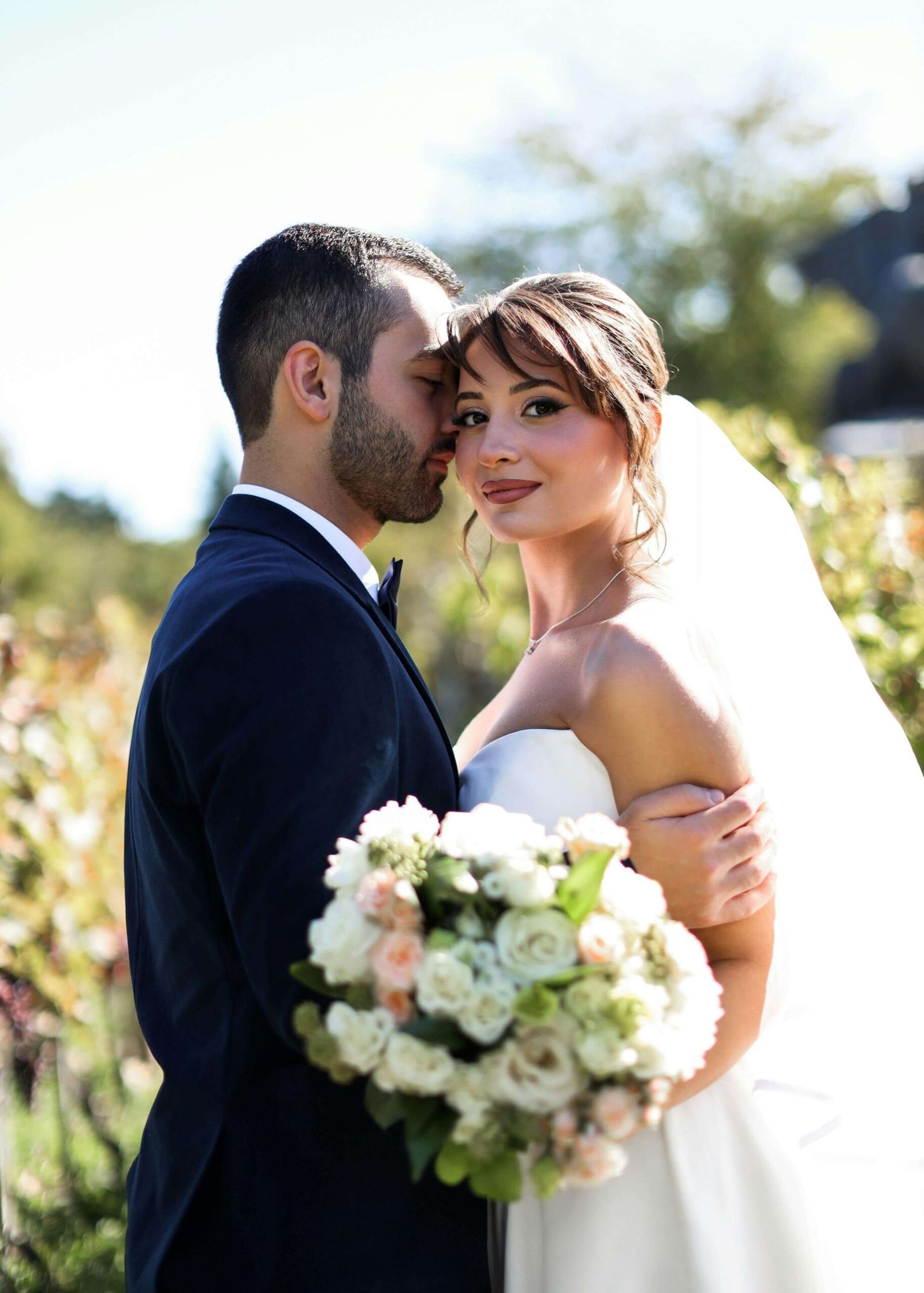 Couple in formal clothing standing close outdoors, one person holding a white bouquet.