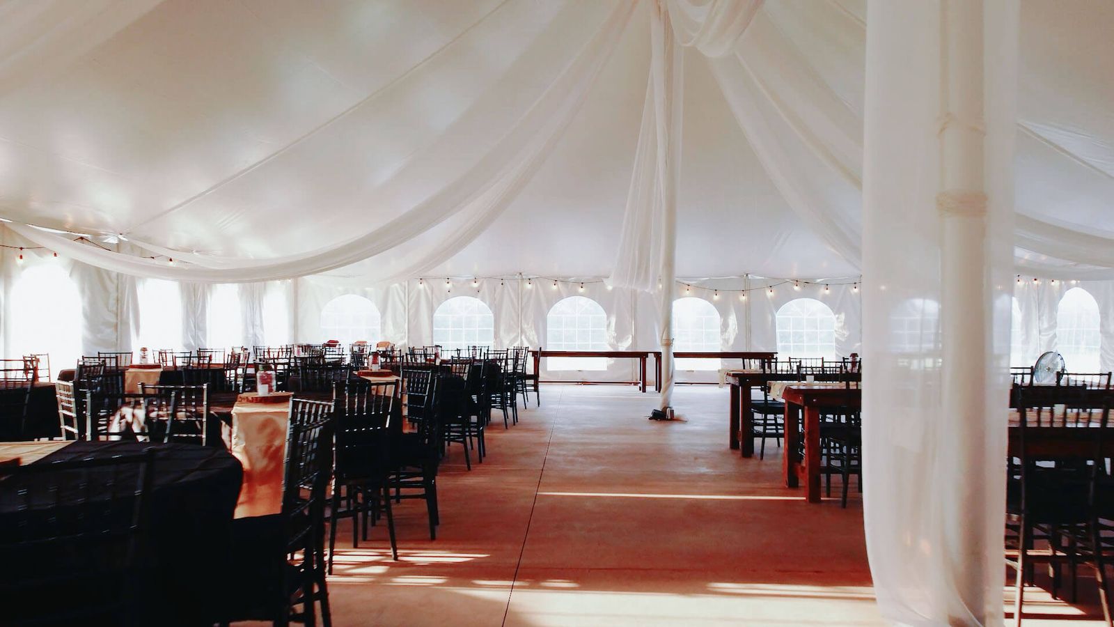 Draped Tent Interior Empty white-draped tent with rows of dark chairs and red flooring.