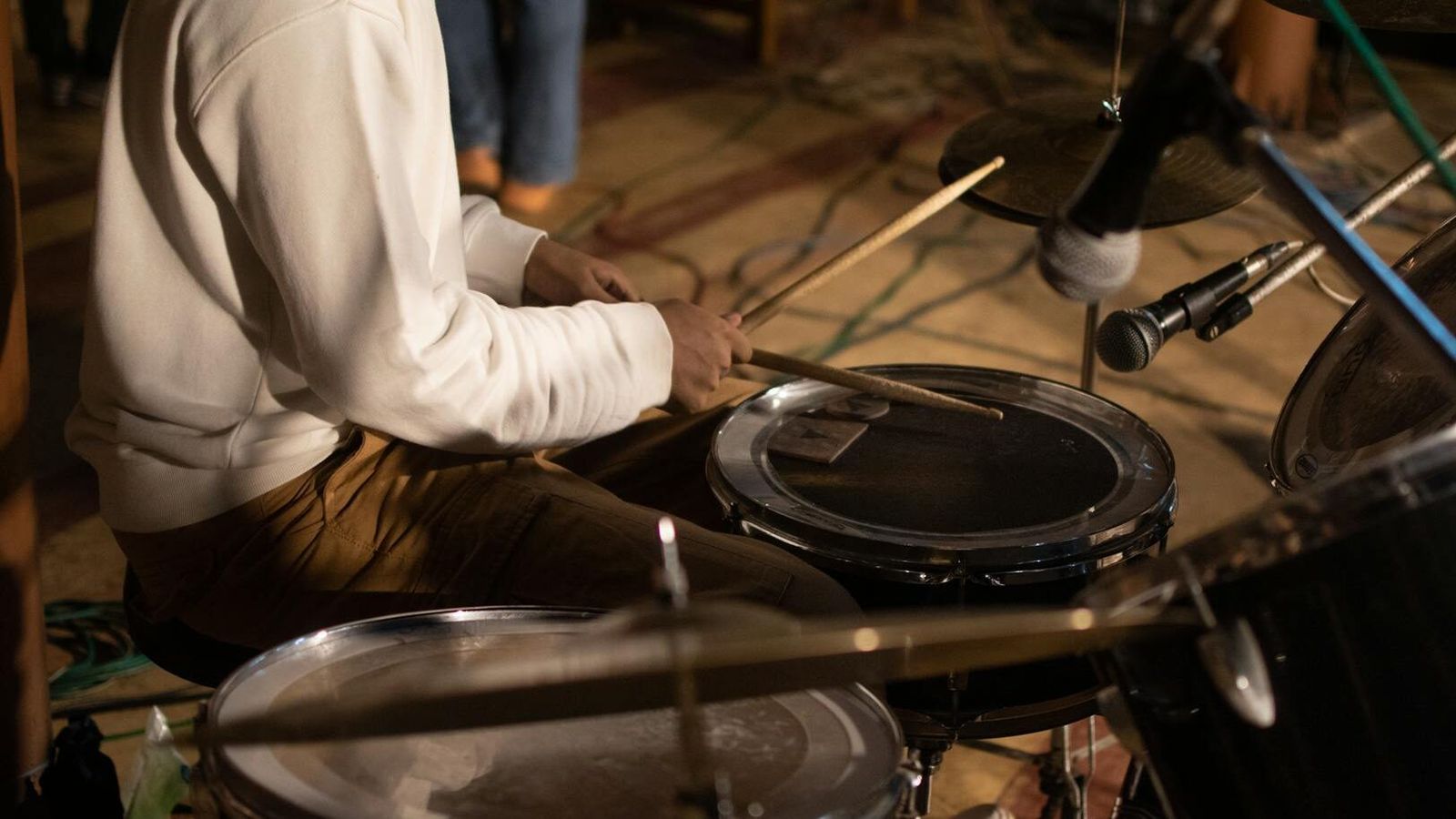 Seated drummer playing a drum kit indoors.