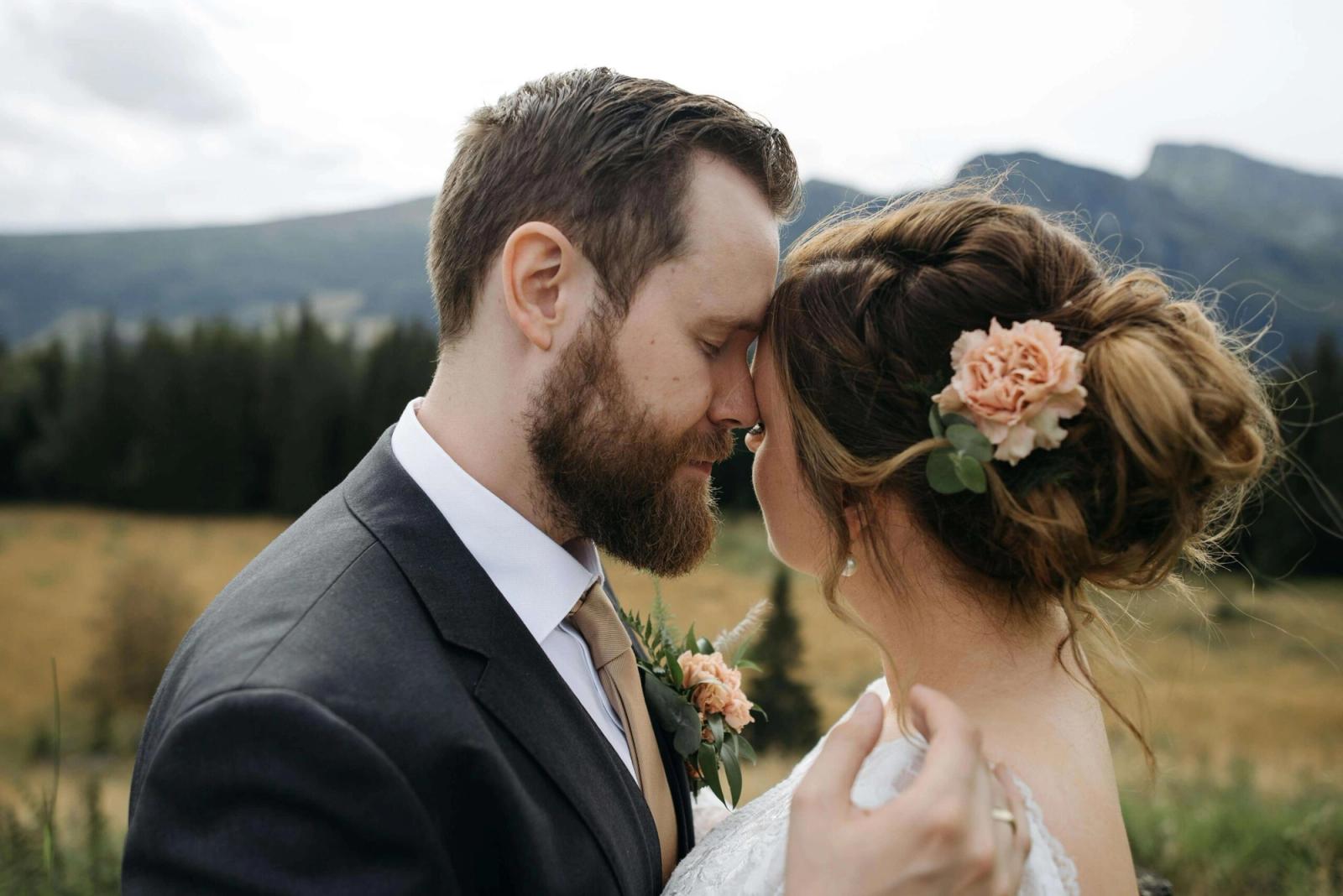 Close portrait of a couple in formal clothing touching foreheads, with mountains behind.