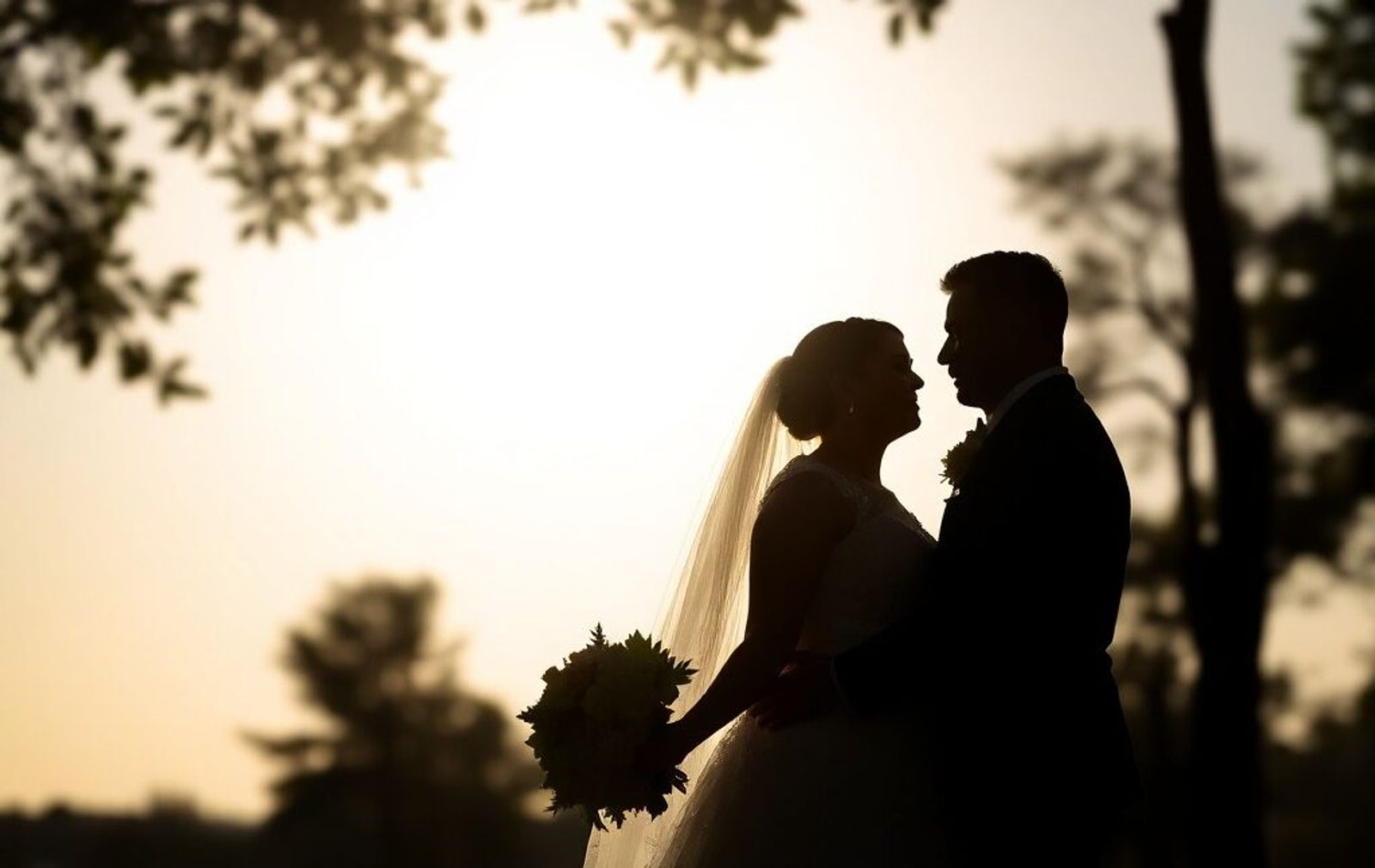 Silhouetted couple facing each other against a bright sunset.