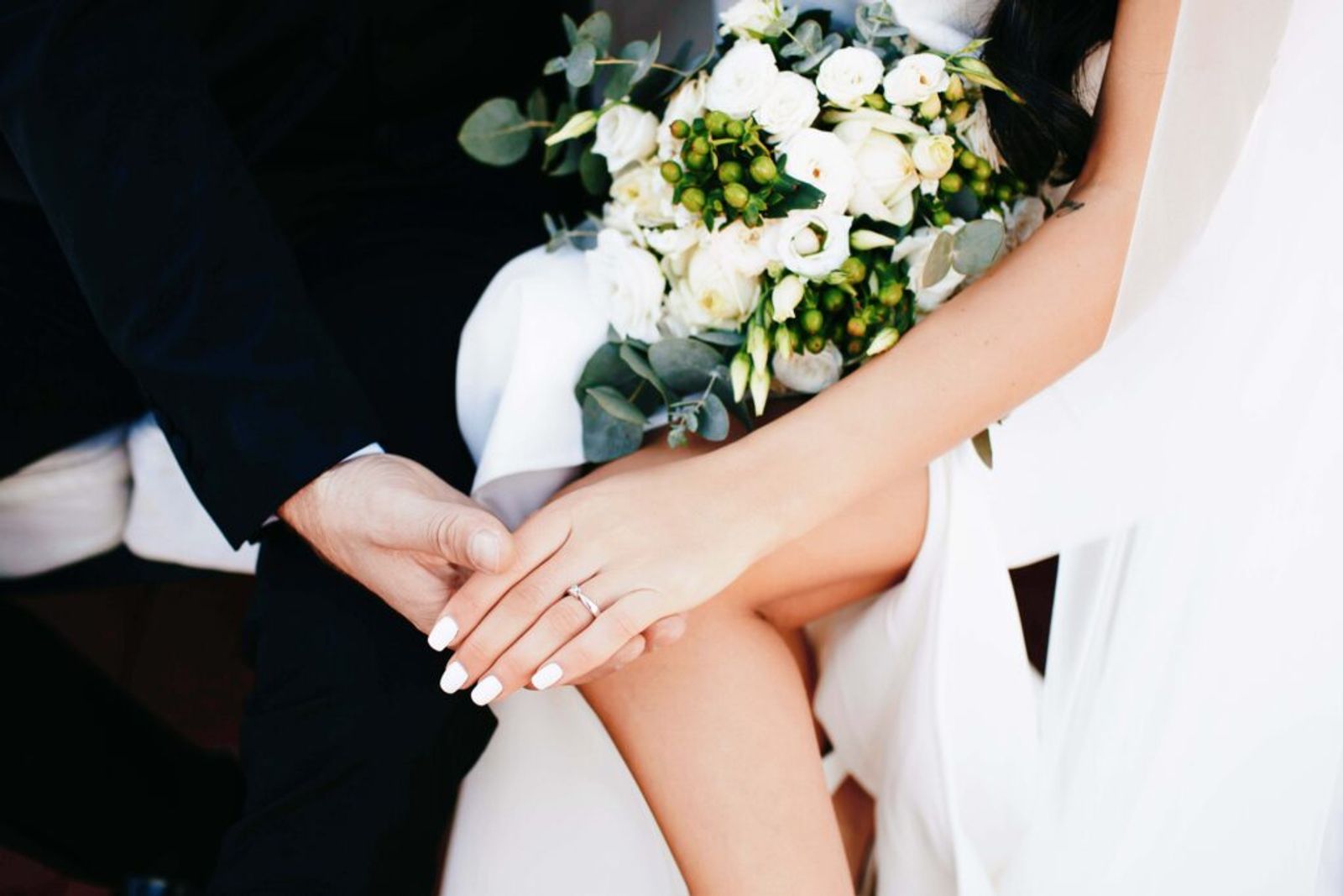 Close crop of two seated people holding hands, with a white bouquet above.