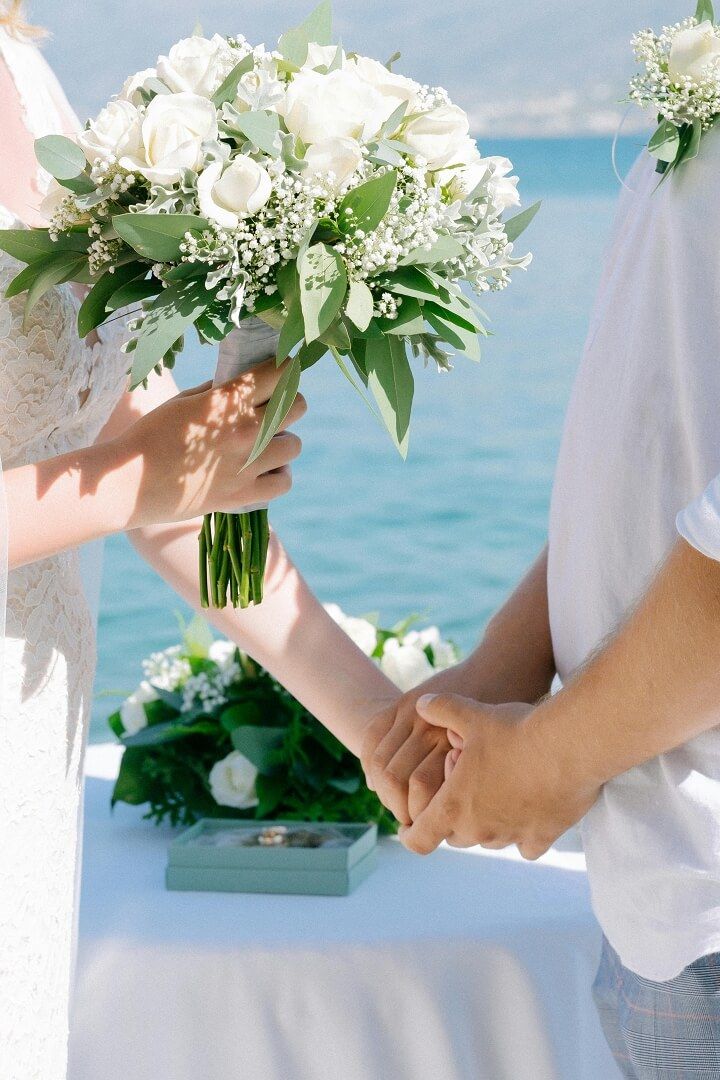 Bouquet And Hands Close crop of a white bouquet held above two joined hands near water.