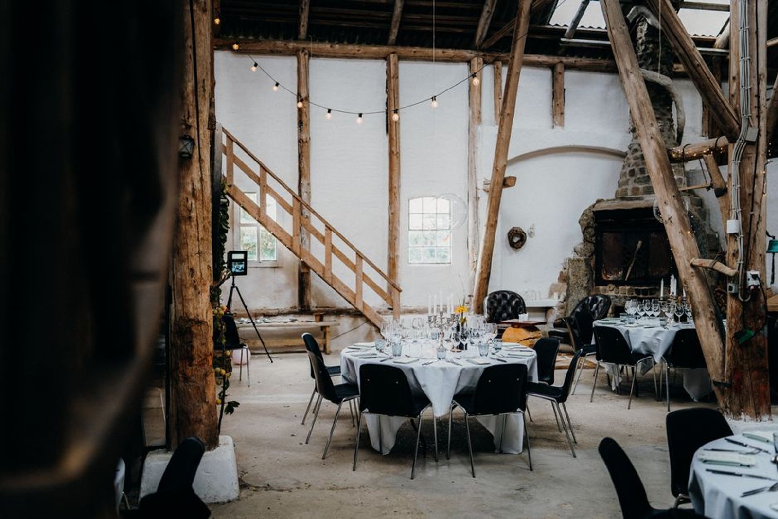 Partly unfinished industrial room with exposed framing and a few set dining tables.