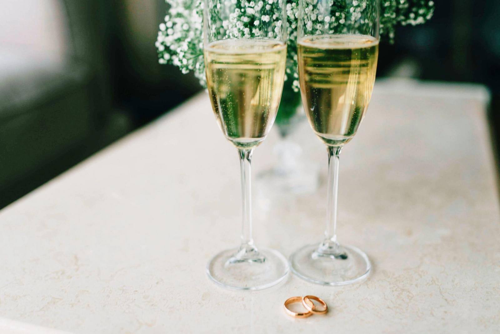 Two champagne flutes and two rings on a pale stone surface.