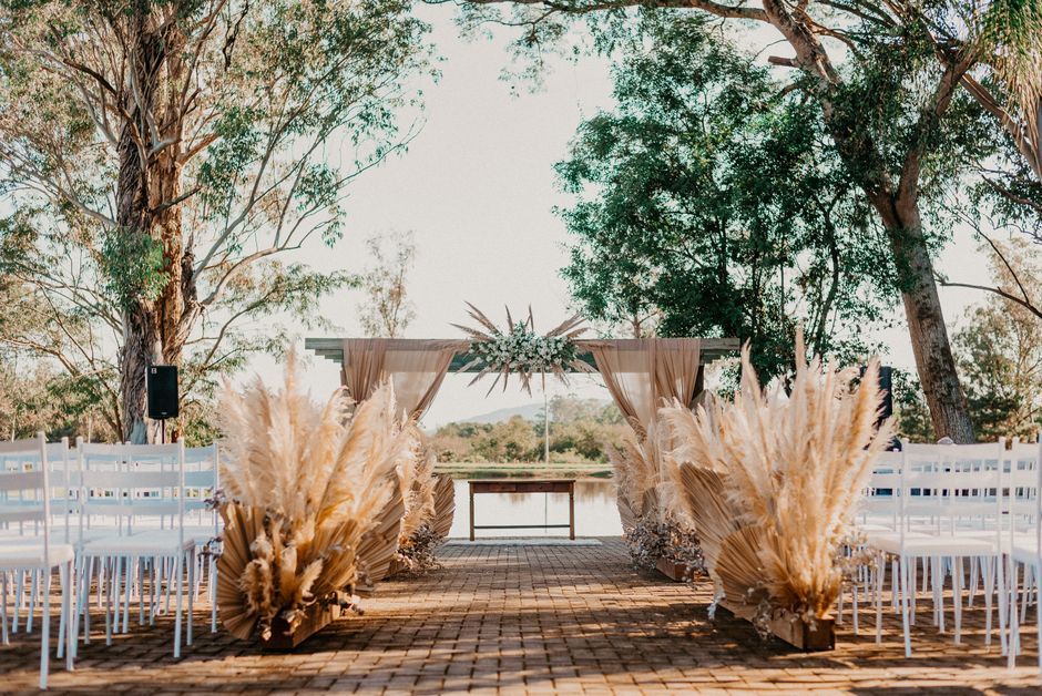 Pampas Ceremony Aisle Empty outdoor ceremony aisle framed by pampas grass, trees, and white chairs.