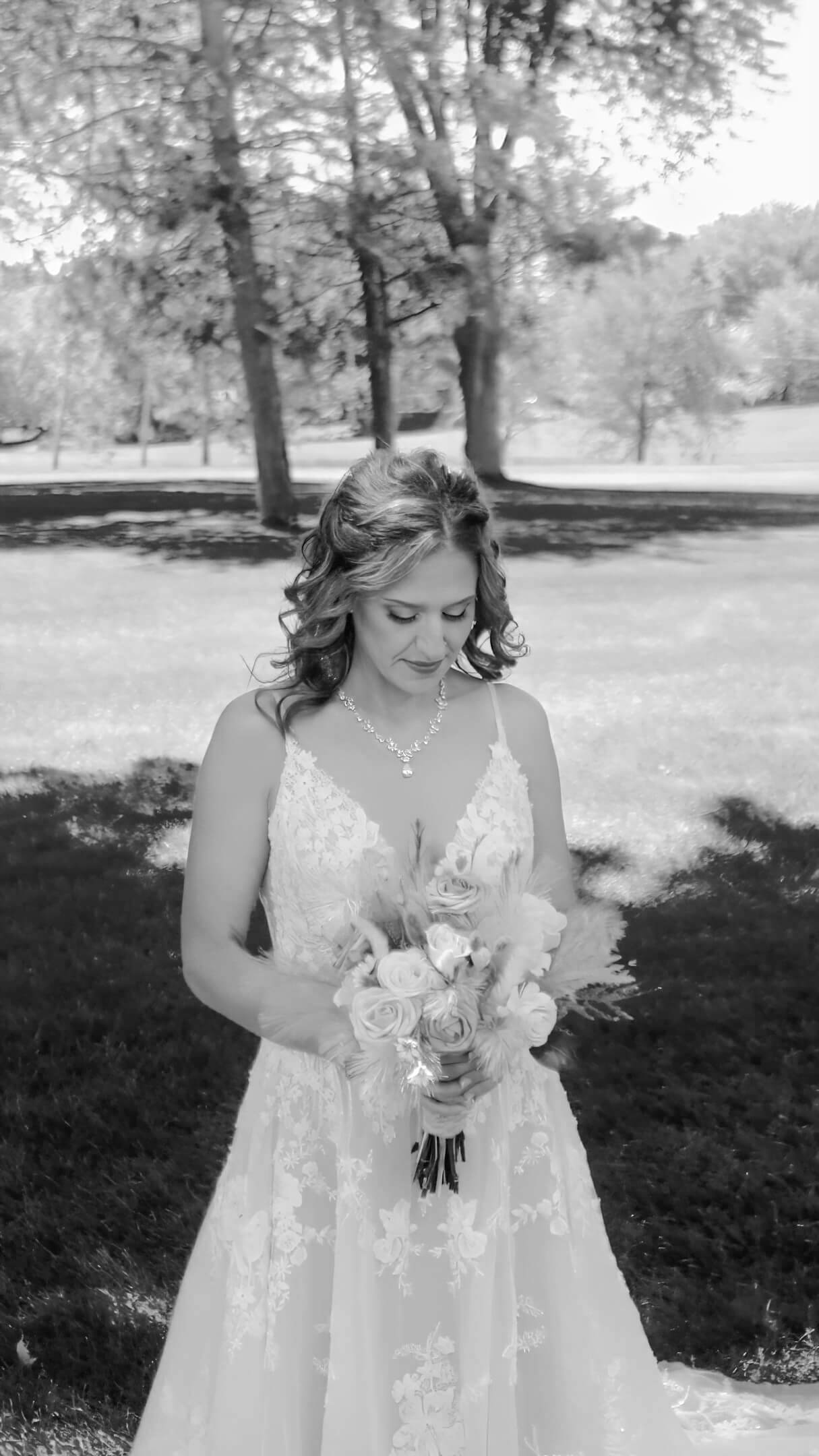 Black-and-white portrait of a person in a white dress holding a bouquet outdoors.