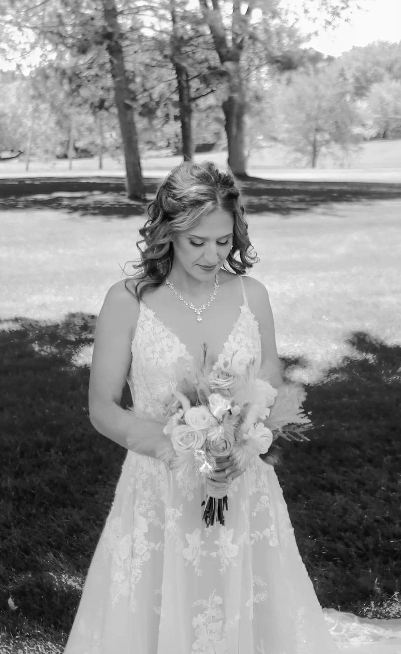Black-and-white portrait of a person in a white dress holding a bouquet outdoors.