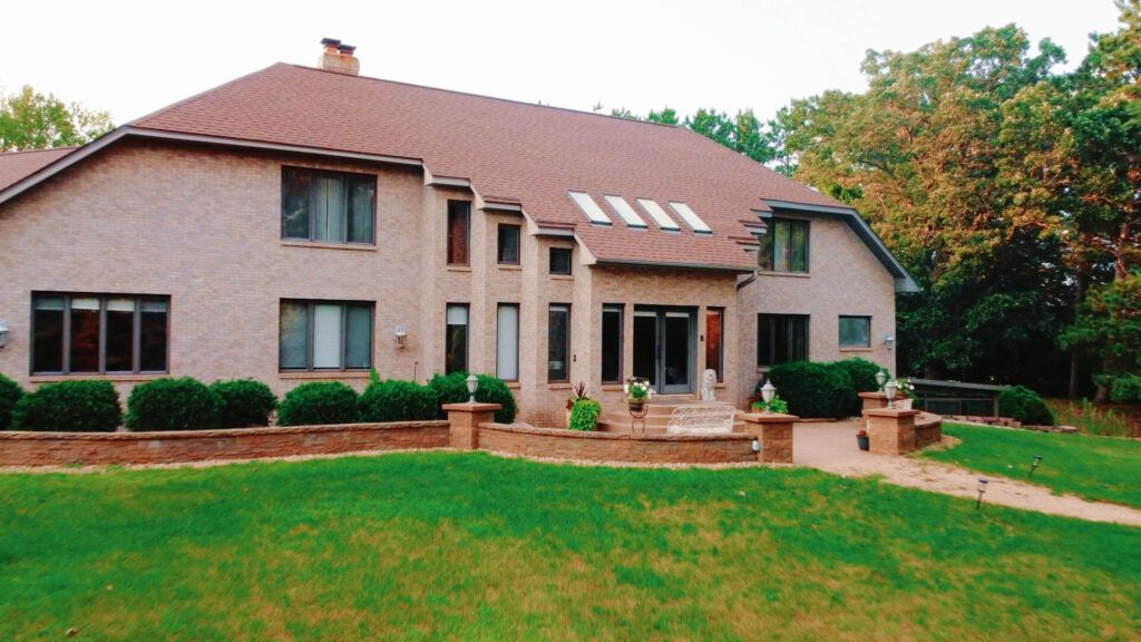 Large Country House Large beige house with a red roof, patio, lawn, and surrounding trees.