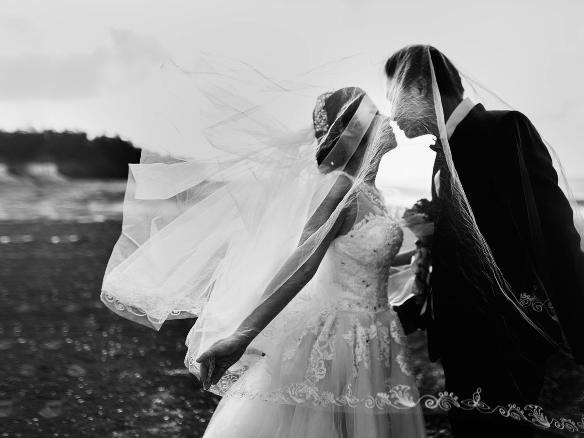 Windblown Veil Black-and-white portrait of a couple kissing beneath a windblown veil.