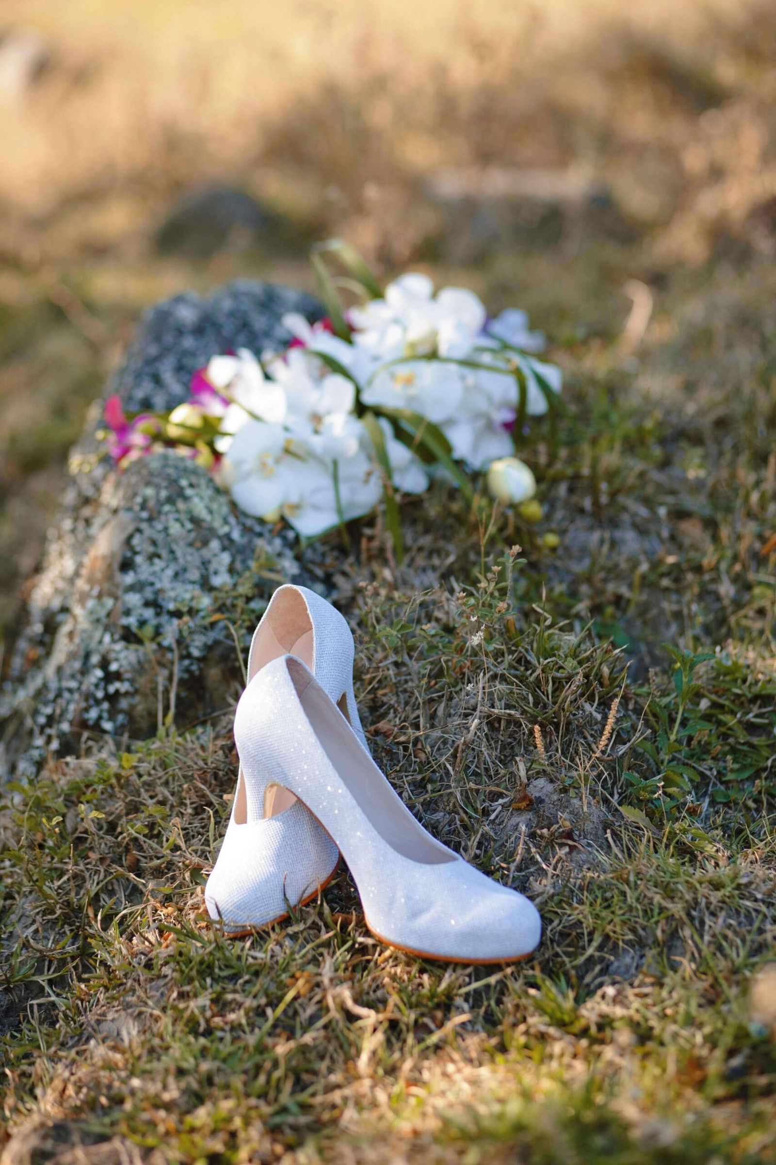 White heels and a white bouquet resting on grass.