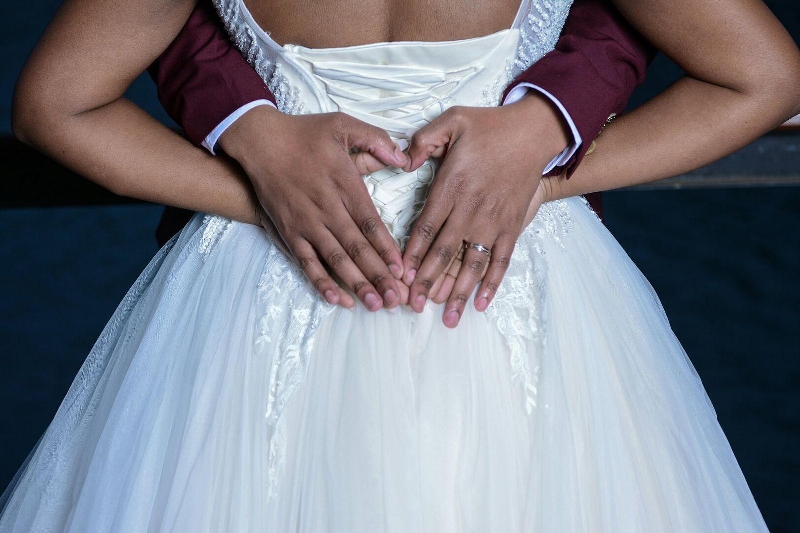 Close crop of two hands forming a heart shape over a white dress.