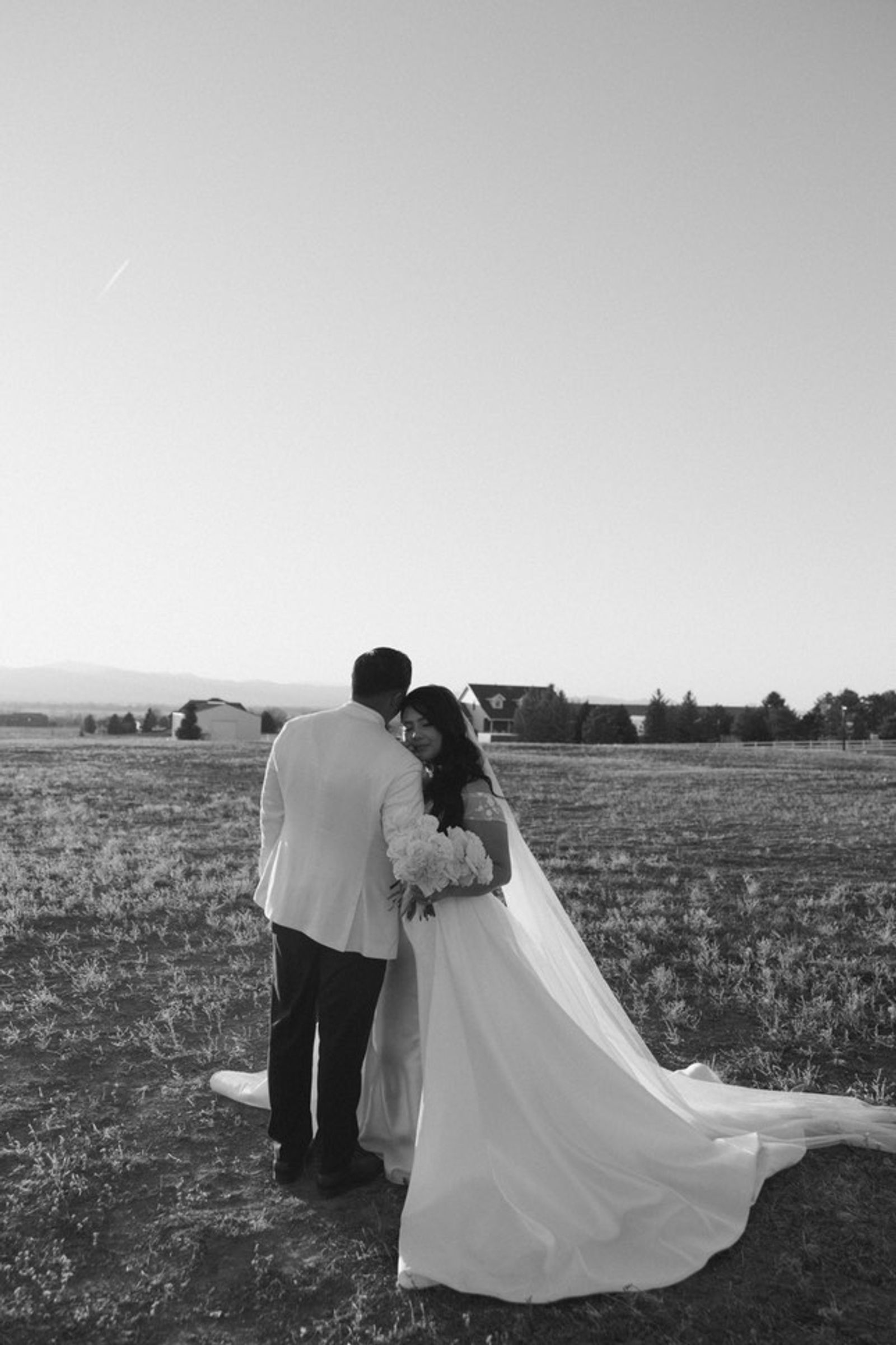 Black-and-white rear view of a couple in formal clothing standing in an open field.