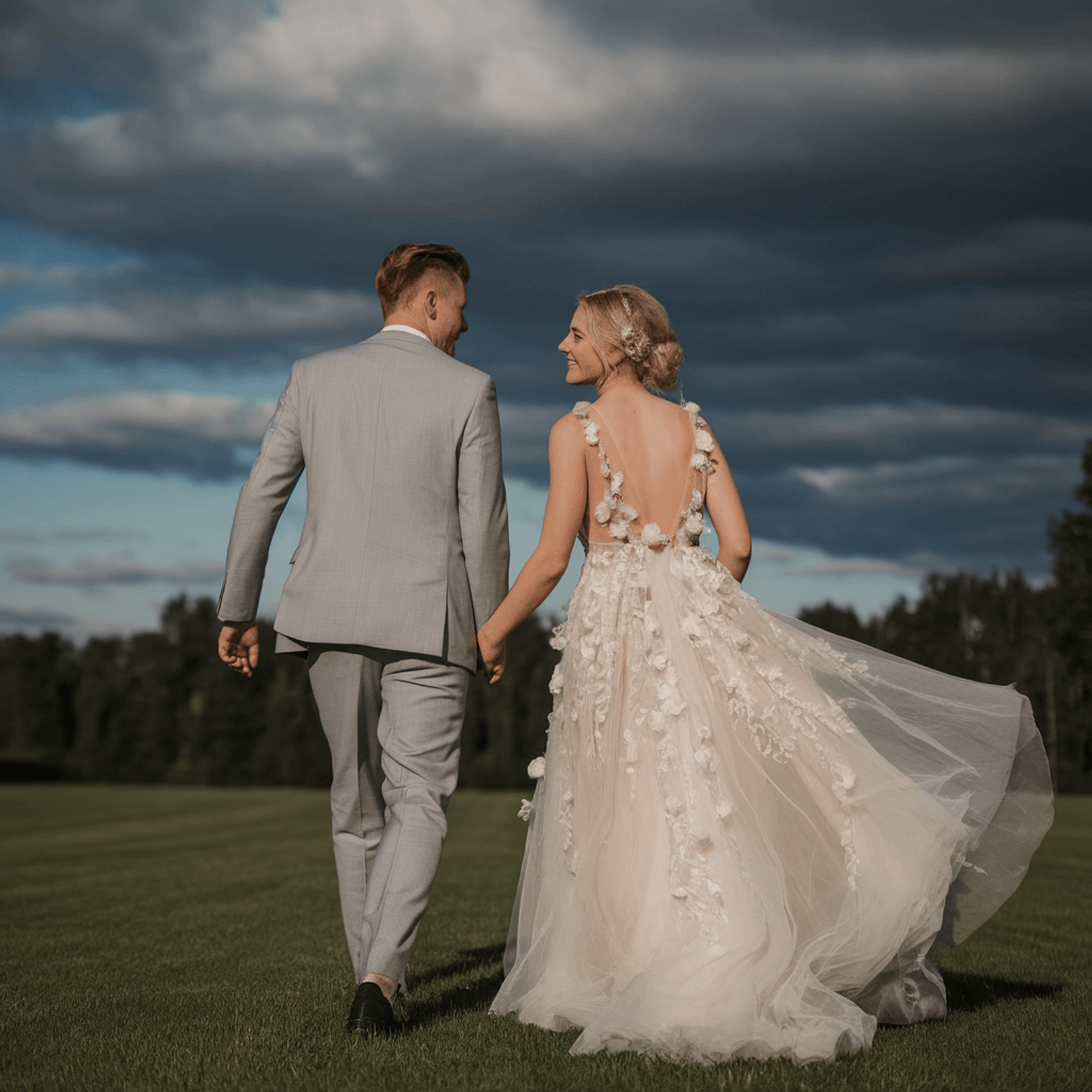 Couple in formal clothing walking hand in hand beneath dark clouds.