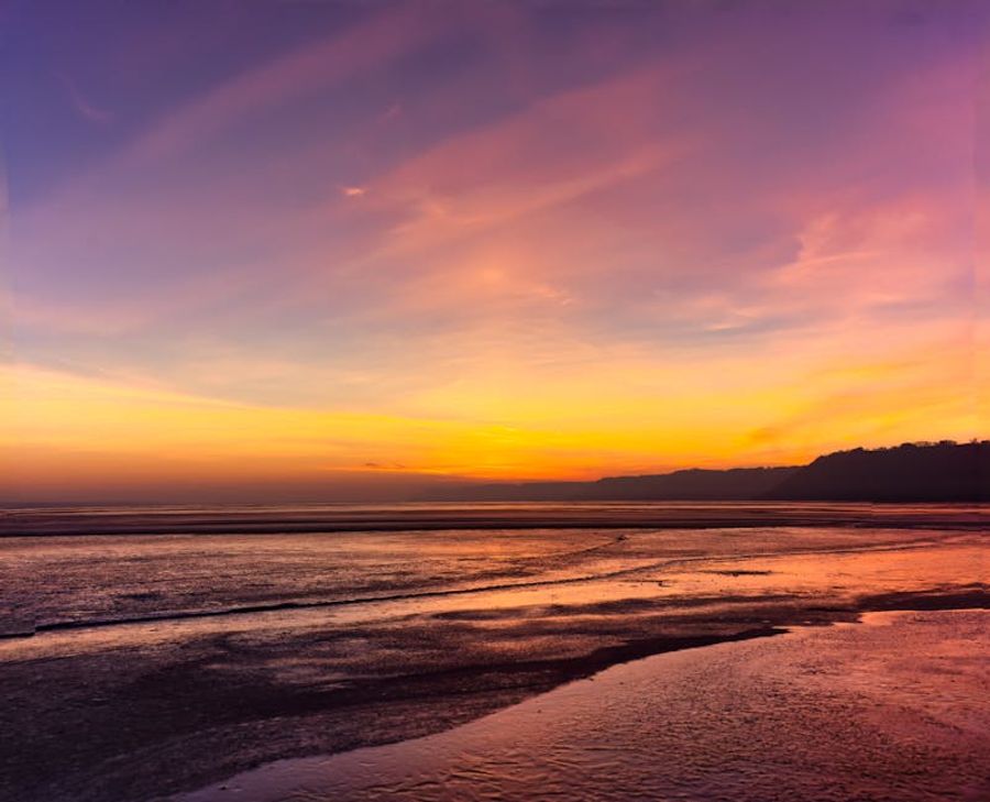 Orange and purple sunset over waves along a shoreline.