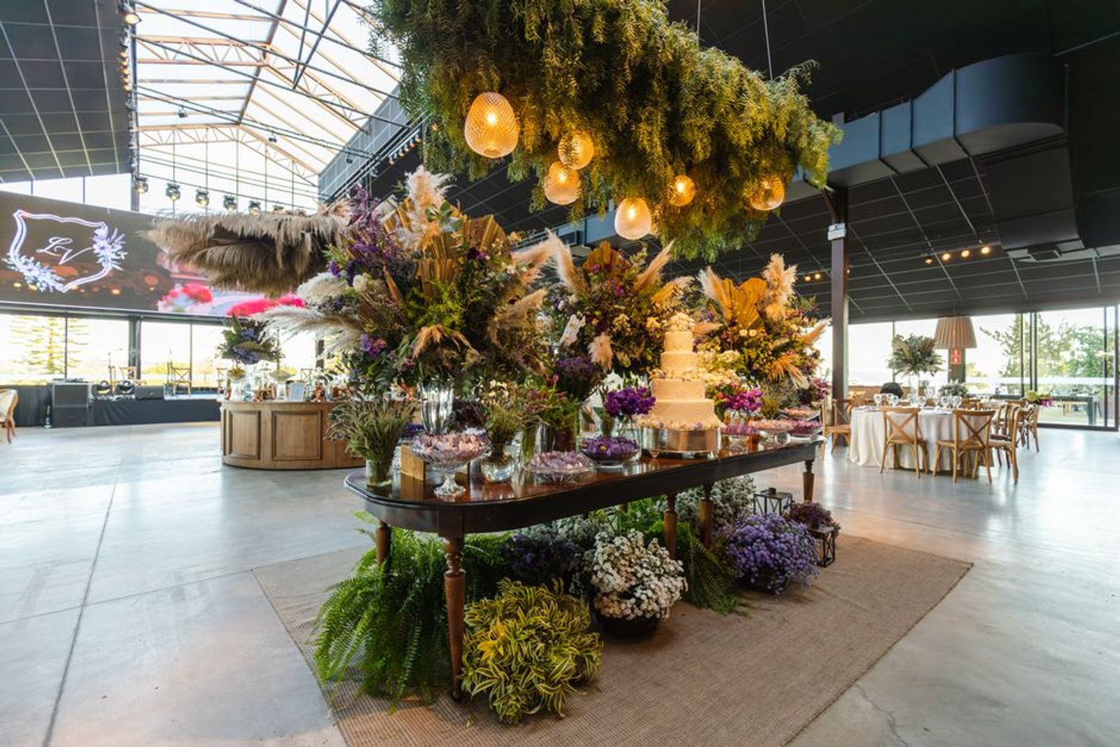 Large indoor floral installation and display table beneath a glass roof.