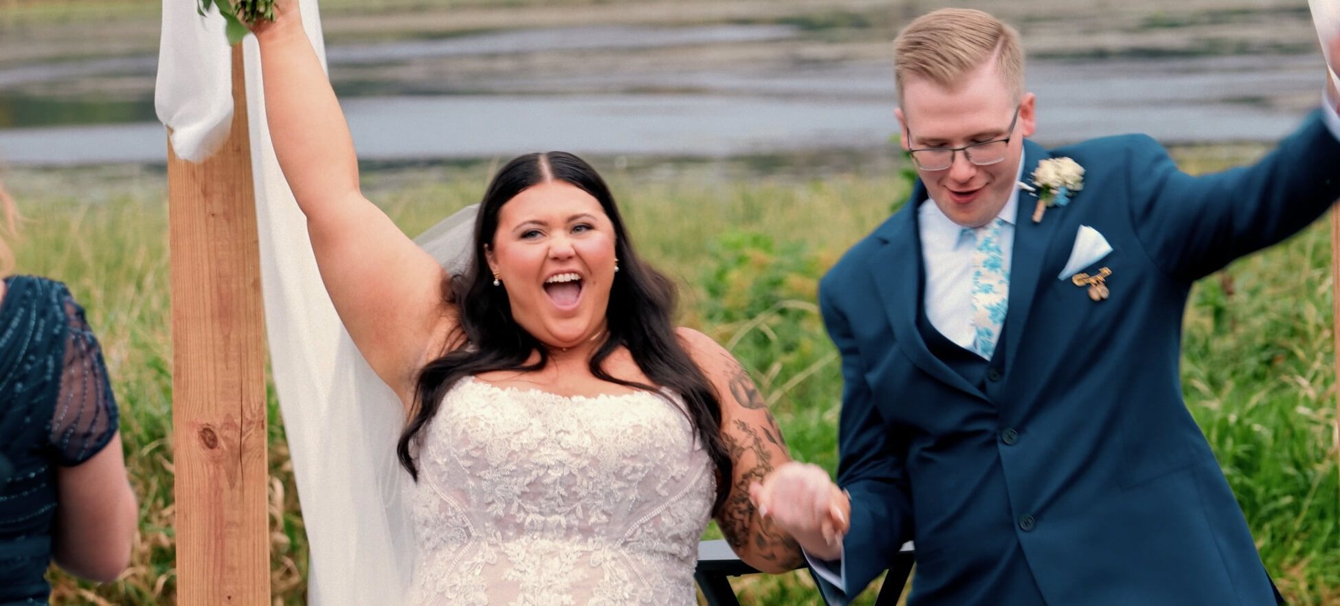 Raised Arms Duplicate Two formally dressed people holding hands with their free arms raised outdoors.