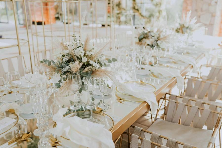 White Reception Room Bright dining room filled with white tables, glassware, pale flowers, and gold chairs.