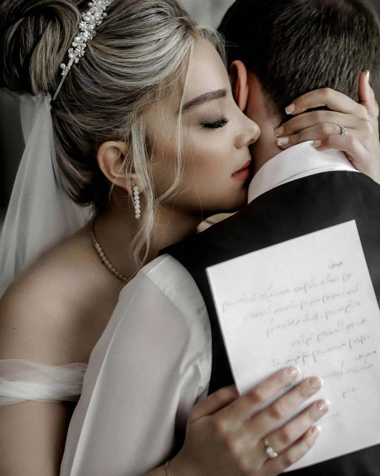 Letter and Embrace Person in a white wedding dress kisses a person in a dark suit while holding a handwritten letter.