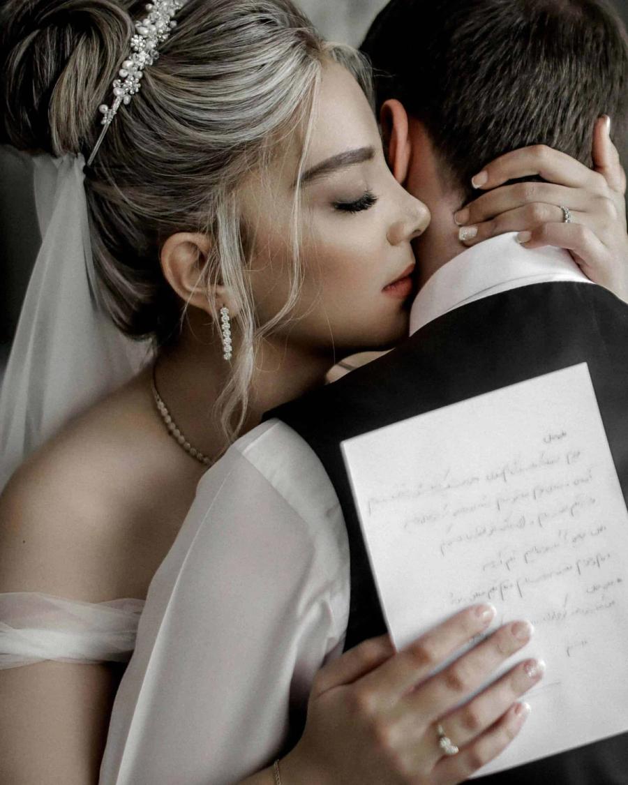 Letter and Embrace Person in a white wedding dress kisses a person in a dark suit while holding a handwritten letter.