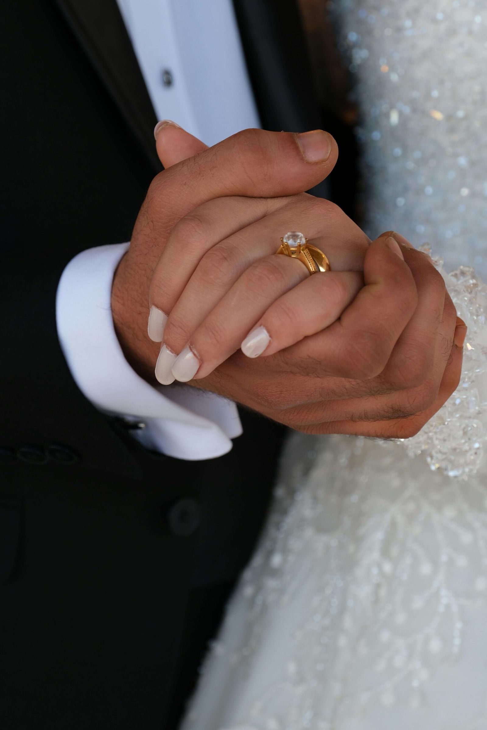Close-up of two clasped hands with a gold ring and white manicure.