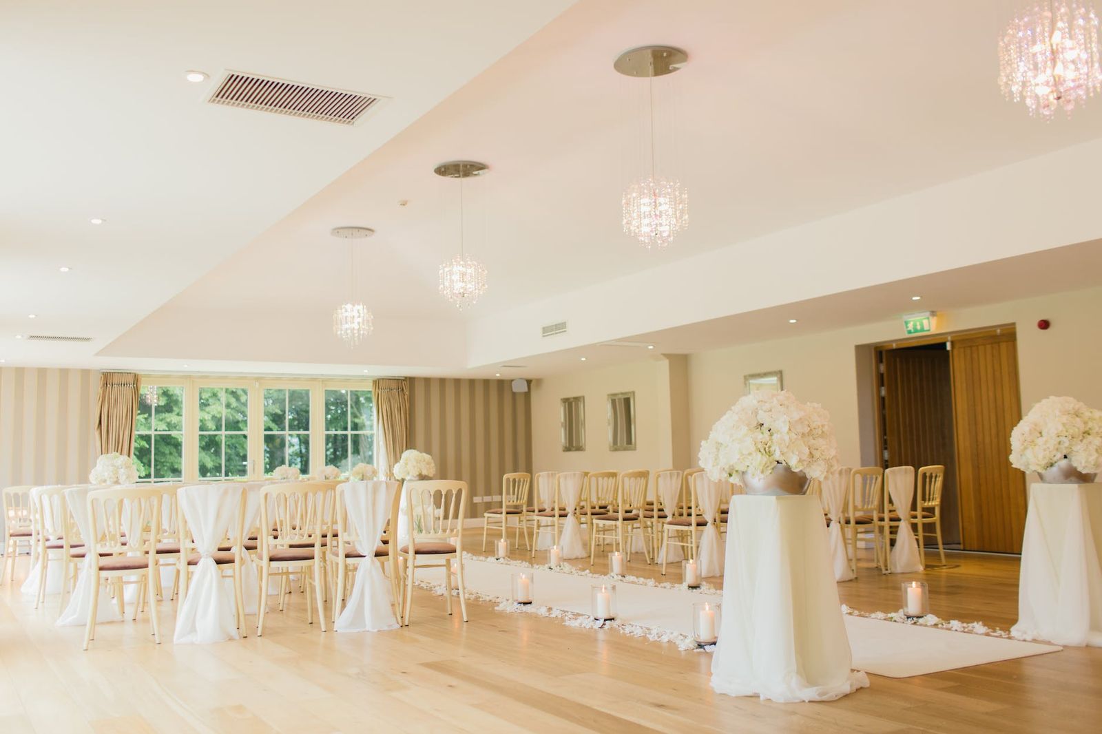 Bright Ceremony Room Bright reception room with white chairs, chandeliers, and a flower-covered ceremony arch.