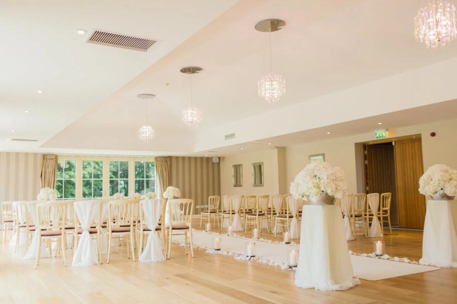 Bright Ceremony Room Bright reception room with white chairs, chandeliers, and a flower-covered ceremony arch.