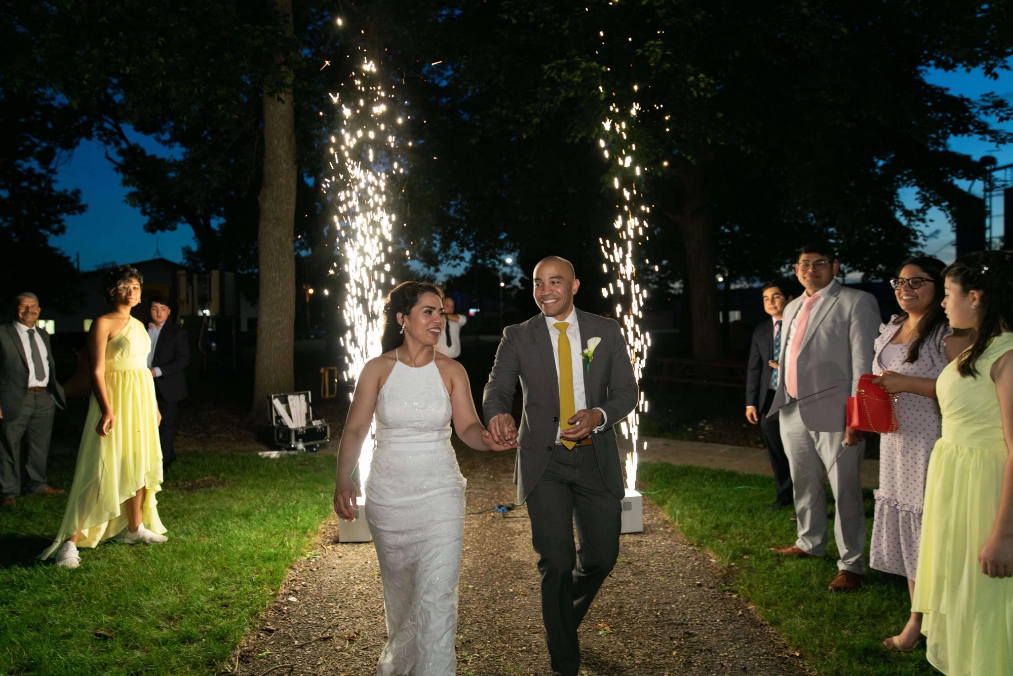 Spark Fountain Walk Two formally dressed people walking along a path between vertical fountains of sparks.