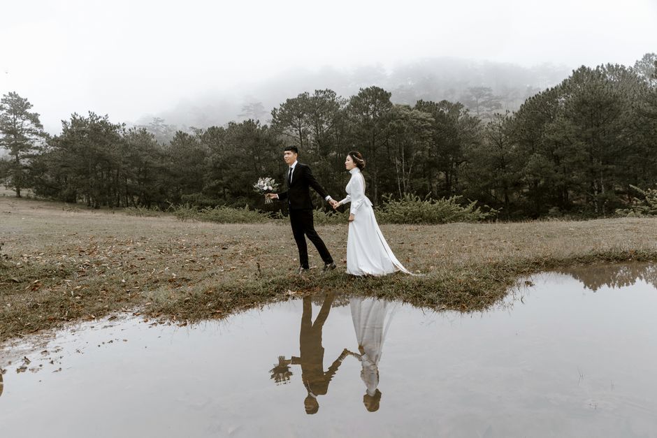 Waterside Walk Couple in wedding attire walking beside water with their reflections visible.