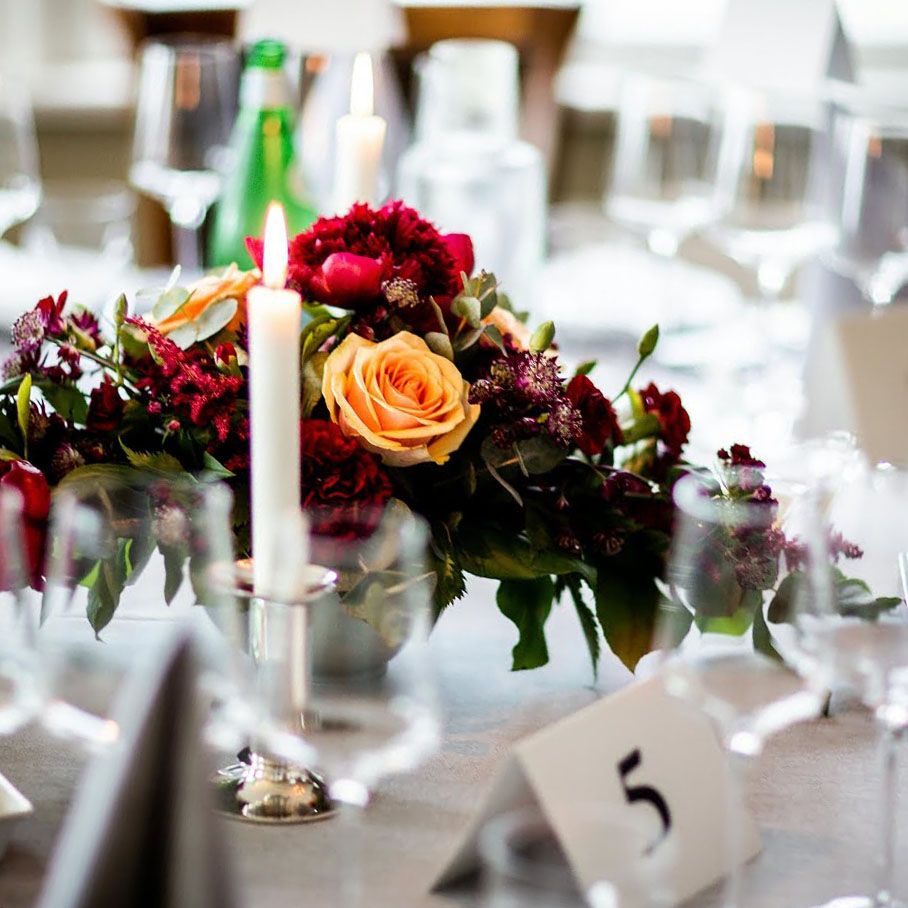 Table Number Five Reception table with red and orange flowers, a candle, glassware, green bottle, and table number five.
