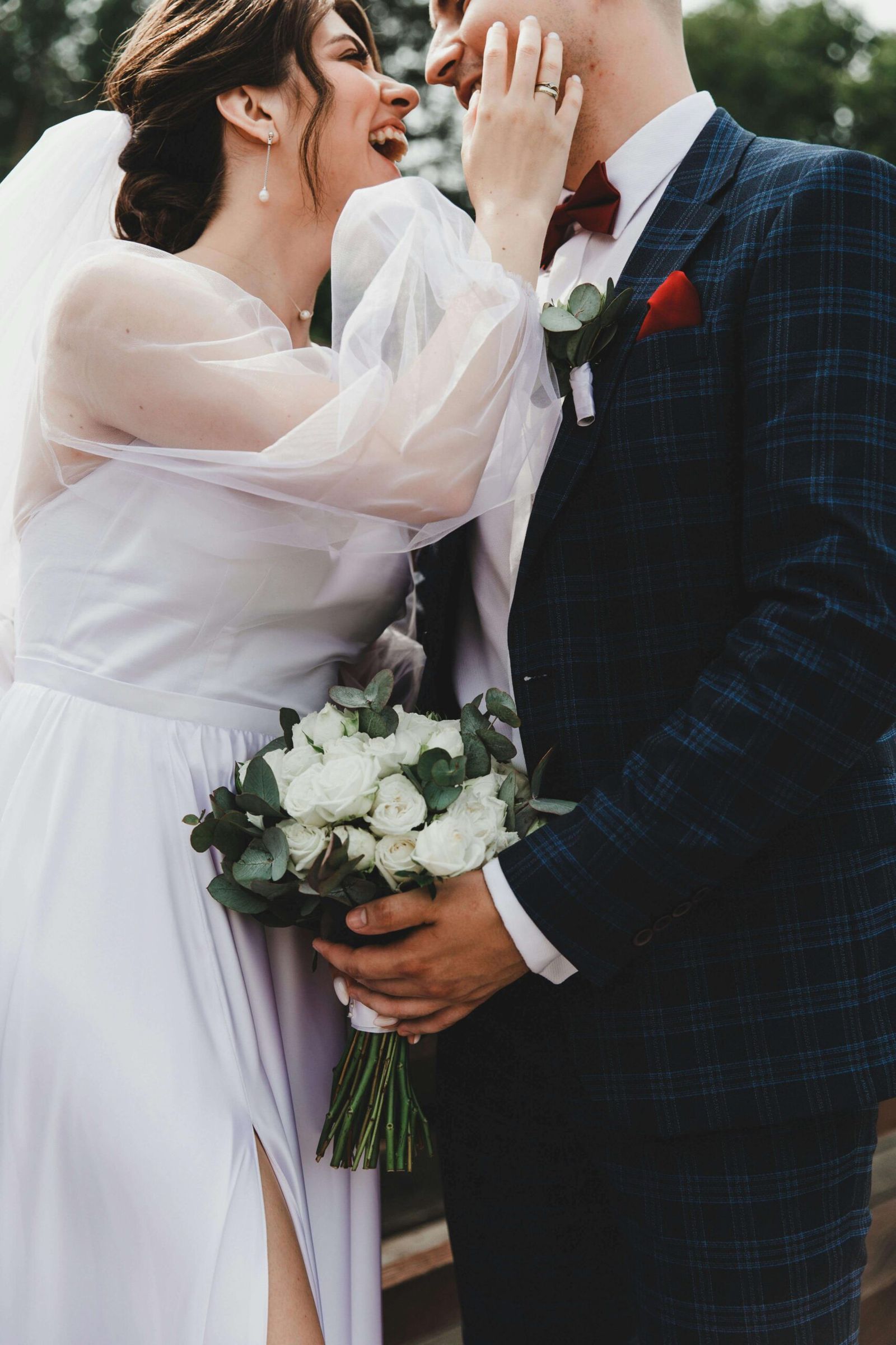 Outdoor Bouquet Embrace Couple in wedding attire embracing outdoors while one holds a bouquet of white flowers.