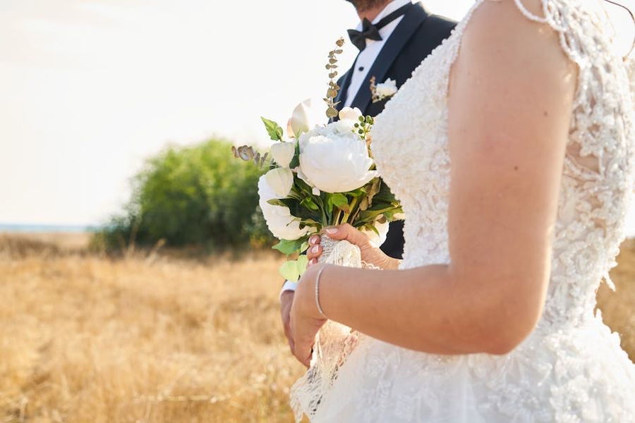 White Rose Bouquet Close crop of two people in wedding attire, including a white lace dress and a white rose bouquet.