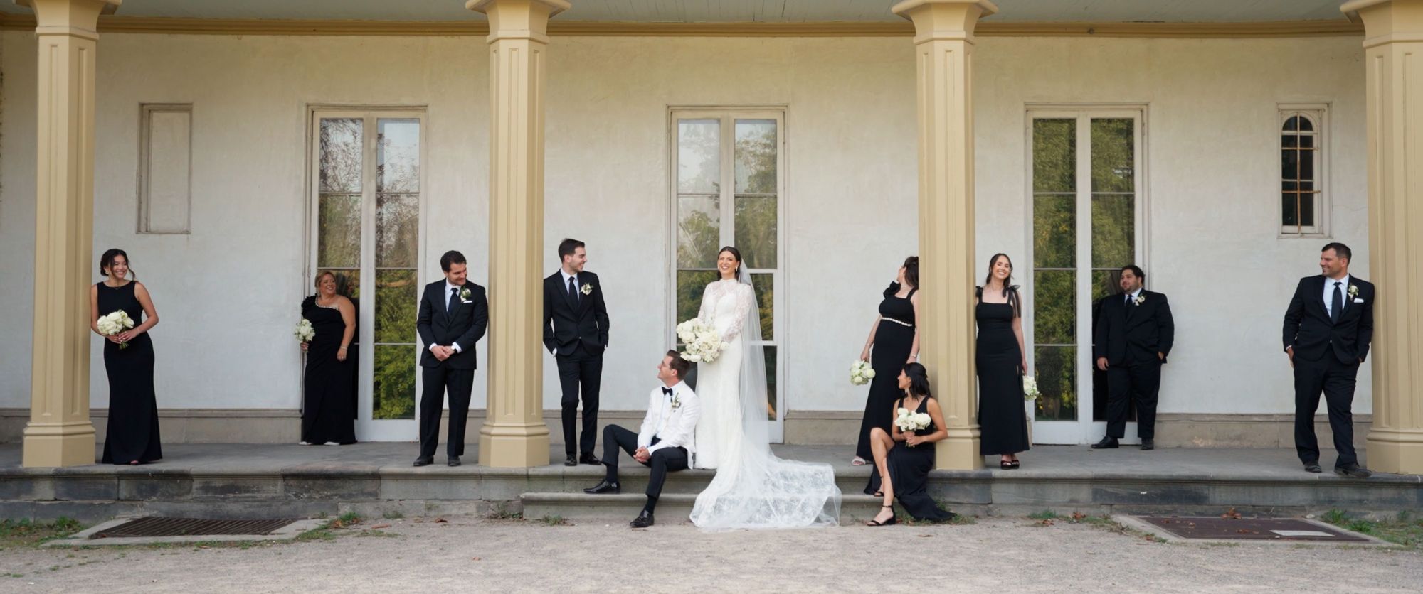 Columned Porch Group Formal group spaced along a covered porch with columns, centered around a person in a white dress.