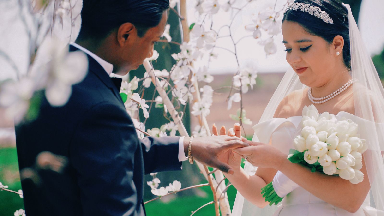 Ring Exchange Close-up of hands exchanging a ring beside white blossoms.