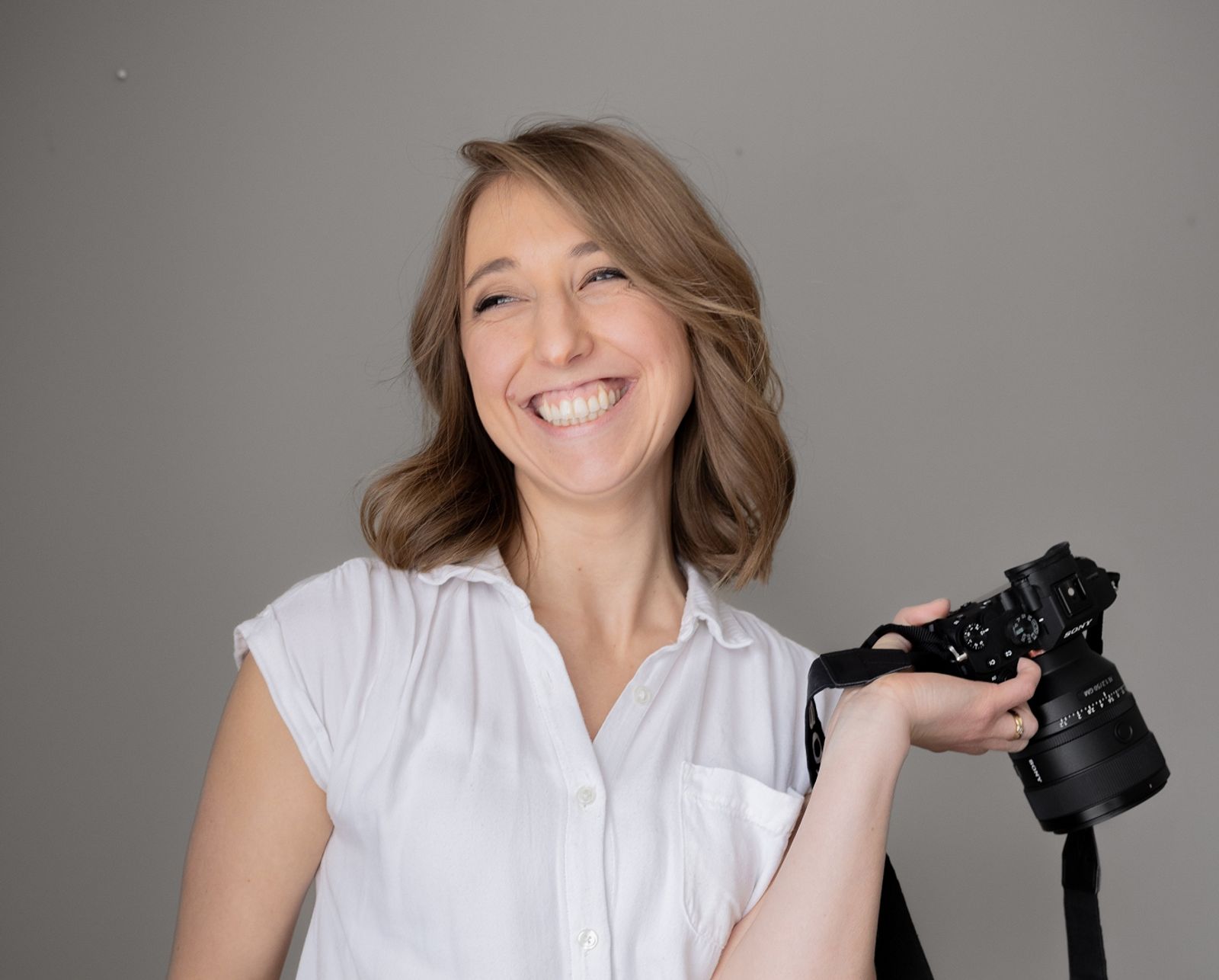 Camera Portrait Smiling person holding a camera against a plain gray backdrop.